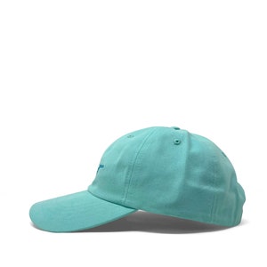 Custom embroidered script hat with personalized text on teal cotton twill dad cap featuring unstructured low profile shape and adjustable strap closure. Clean stitched lettering design on front panel suitable for branding, custom text display and everyday wear. Soft breathable cotton fabric with curved visor and detailed embroidery finish.