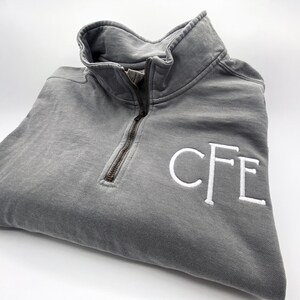 May include: A gray quarter-zip sweatshirt with a white embroidered monogram "CFE" on the right side.