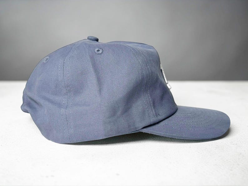 Custom embroidered question mark hat on blue cotton 5 panel snapback cap featuring structured crown and pre curved visor. Clean white embroidery symbol on front panel suitable for custom text, logo placement and daily wear. Adjustable snapback closure provides flexible fit with breathable cotton twill fabric. Product mockup shows front view on neutral background highlighting stitching detail, panel structure and consistent composition for all listing images.