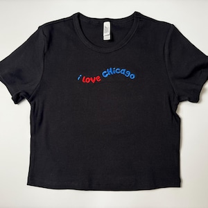Custom embroidered baby tee for women in soft ribbed cotton, featuring personalized text on a fitted cropped American Apparel shirt. This trendy y2k baby tee showcases minimal embroidery design, perfect for aesthetic outfits, custom gifts, and everyday wear. Styled in a clean neutral background to highlight the flattering stretch fit, short sleeves, and modern cropped silhouette, ideal for fashion brands, casual styling, and personalized clothing collections.