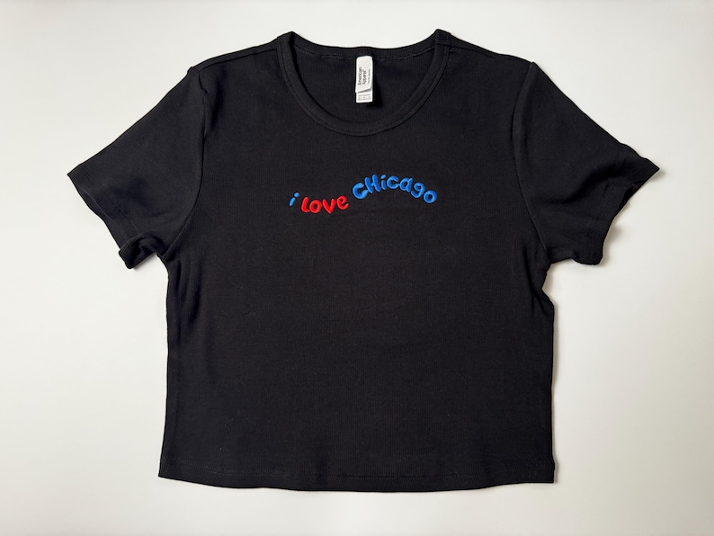 Custom embroidered baby tee for women in soft ribbed cotton, featuring personalized text on a fitted cropped American Apparel shirt. This trendy y2k baby tee showcases minimal embroidery design, perfect for aesthetic outfits, custom gifts, and everyday wear. Styled in a clean neutral background to highlight the flattering stretch fit, short sleeves, and modern cropped silhouette, ideal for fashion brands, casual styling, and personalized clothing collections.