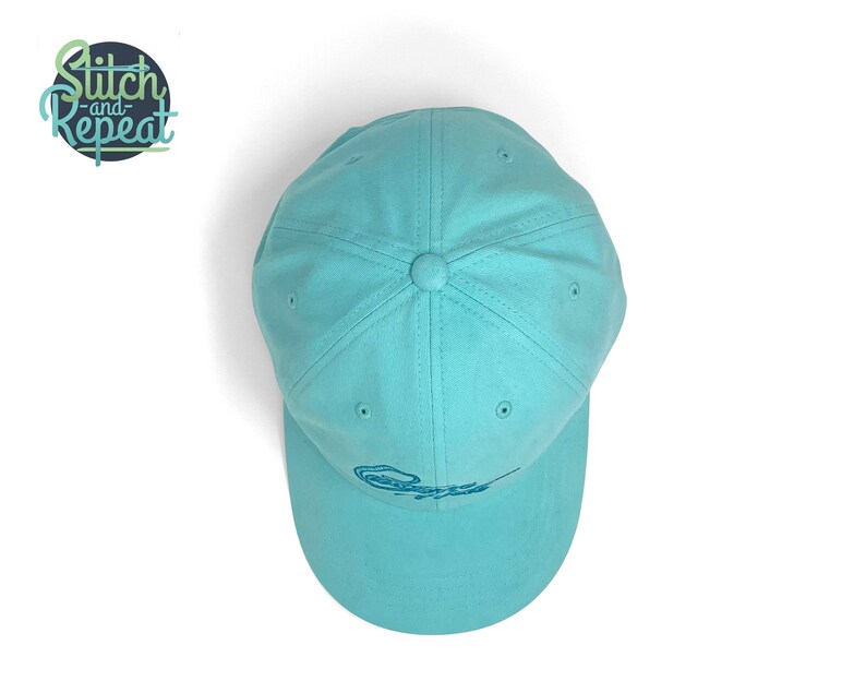 Custom embroidered script hat with personalized text on teal cotton twill dad cap featuring unstructured low profile shape and adjustable strap closure. Clean stitched lettering design on front panel suitable for branding, custom text display and everyday wear. Soft breathable cotton fabric with curved visor and detailed embroidery finish.