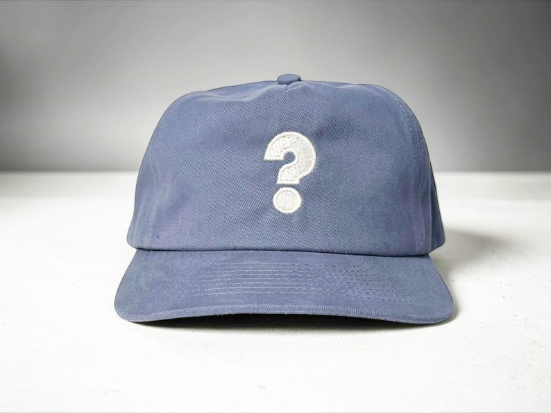 Custom embroidered question mark hat on blue cotton 5 panel snapback cap featuring structured crown and pre curved visor. Clean white embroidery symbol on front panel suitable for custom text, logo placement and daily wear. Adjustable snapback closure provides flexible fit with breathable cotton twill fabric. Product mockup shows front view on neutral background highlighting stitching detail, panel structure and consistent composition for all listing images.