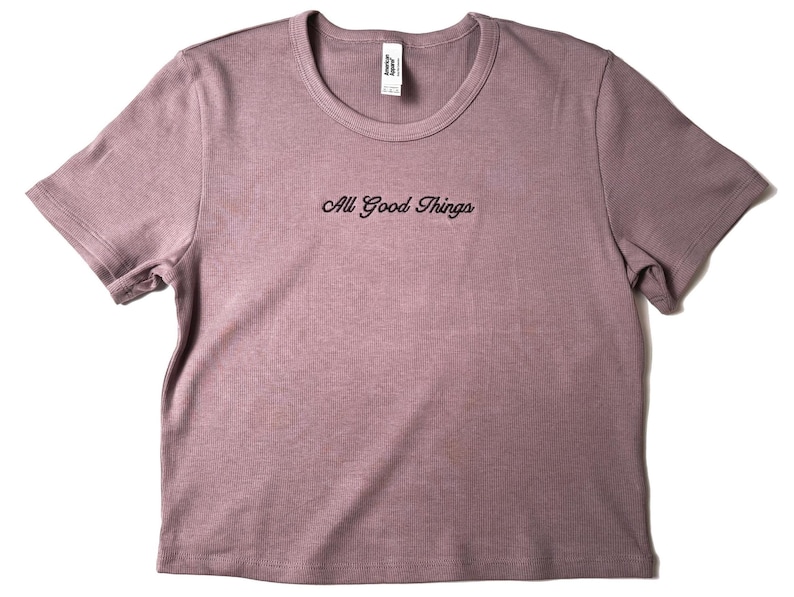 Custom embroidered baby tee for women in soft ribbed cotton, featuring personalized text on a fitted cropped American Apparel shirt. This trendy y2k baby tee showcases minimal embroidery design, perfect for aesthetic outfits, custom gifts, and everyday wear. Styled in a clean neutral background to highlight the flattering stretch fit, short sleeves, and modern cropped silhouette, ideal for fashion brands, casual styling, and personalized clothing collections.