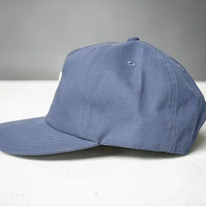 Custom embroidered question mark hat on blue cotton 5 panel snapback cap featuring structured crown and pre curved visor. Clean white embroidery symbol on front panel suitable for custom text, logo placement and daily wear. Adjustable snapback closure provides flexible fit with breathable cotton twill fabric. Product mockup shows front view on neutral background highlighting stitching detail, panel structure and consistent composition for all listing images.