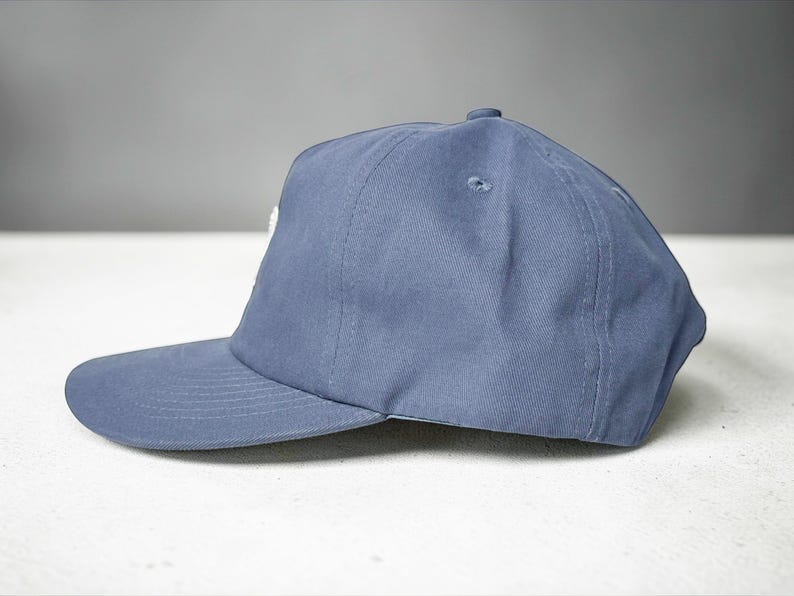 Custom embroidered question mark hat on blue cotton 5 panel snapback cap featuring structured crown and pre curved visor. Clean white embroidery symbol on front panel suitable for custom text, logo placement and daily wear. Adjustable snapback closure provides flexible fit with breathable cotton twill fabric. Product mockup shows front view on neutral background highlighting stitching detail, panel structure and consistent composition for all listing images.