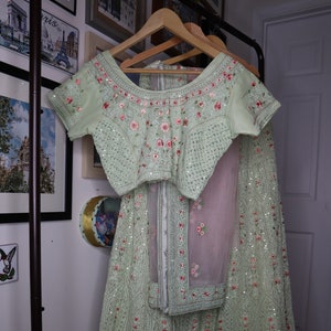 May include: A light green embroidered dress with pink floral details and sequins. The dress has a matching top with short sleeves and a skirt with a sheer overlay.