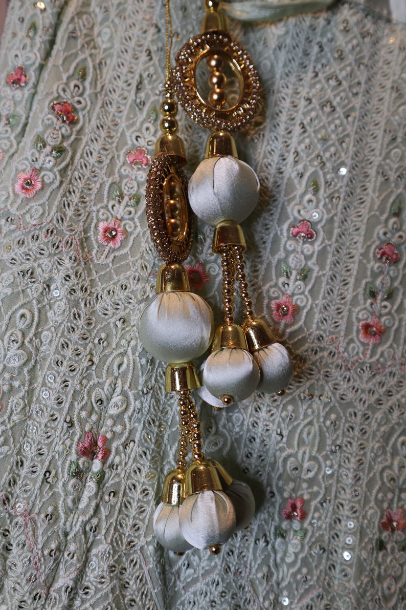 May include: A white fabric with gold and white embellishments. The embellishments are in the shape of round balls and circles. The fabric has a delicate pattern.
