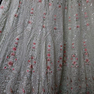 May include: A light green skirt with intricate embroidery and sequins. The skirt features a floral pattern with pink flowers and a paisley border.