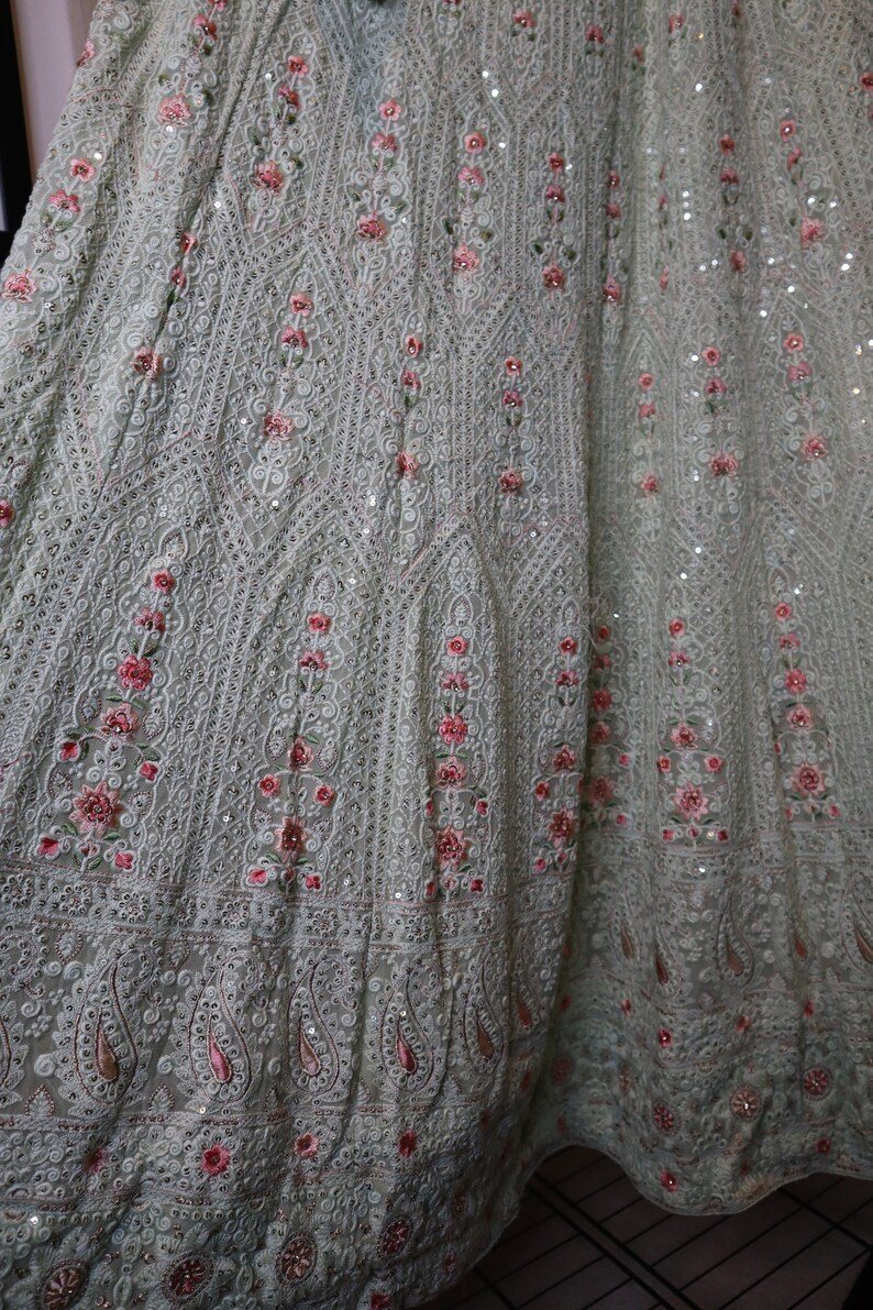 May include: A light green skirt with intricate embroidery and sequins. The skirt features a floral pattern with pink flowers and a paisley border.