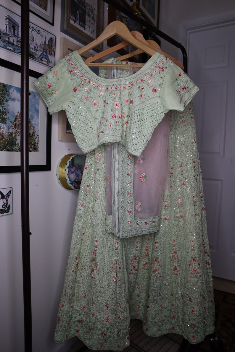 May include: A light green embroidered dress with pink floral details and sequins. The dress has a matching top with short sleeves and a skirt with a sheer overlay.
