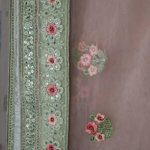 May include: A light green fabric with a border of sequins and floral embroidery. The fabric has a sheer, delicate texture and is adorned with pink and white floral patterns.