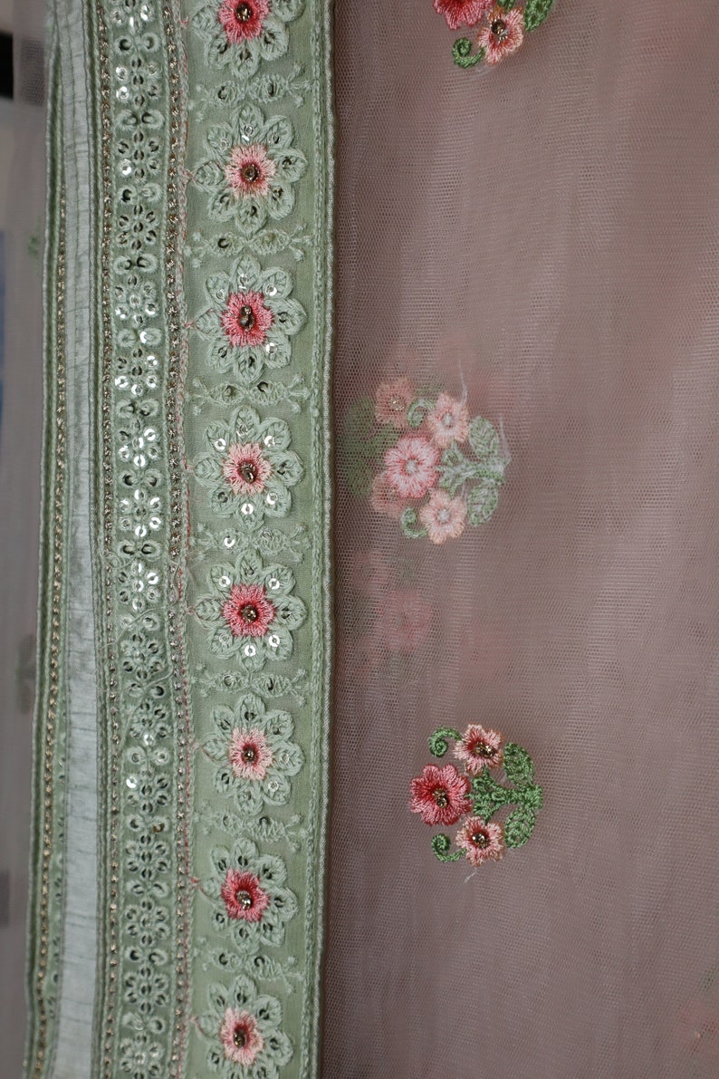 May include: A light green fabric with a border of sequins and floral embroidery. The fabric has a sheer, delicate texture and is adorned with pink and white floral patterns.