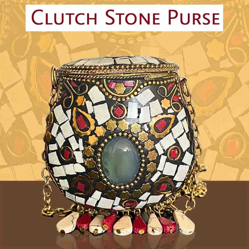 Puede incluir: Un bolso de mano de mosaico blanco y negro con detalles dorados y una piedra verde. El bolso tiene una correa de cadena y detalles de borlas rojas y blancas.