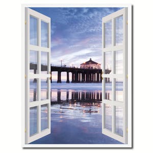 May include: A white window frame with a view of a pier extending into the ocean at sunset. The sky is a soft blue and purple, and the water is a calm blue. The pier has a small building at the end, and there are people walking on it.