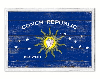 May include: A weathered wooden sign with a blue background and white text. The sign reads "Conch Republic 1828 Key West". A yellow sun with a pink conch shell is in the center of the sign.