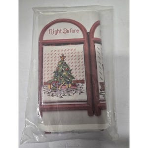 May include: A cross-stitch kit in a clear plastic bag featuring a design of a Christmas tree with presents underneath. The text Night Before is printed in red above the tree. The design is framed by a red archway on a white background.