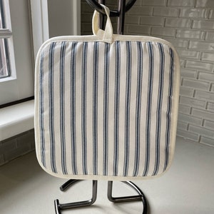 May include: A white pot holder with blue stripes hanging on a black metal pot holder stand.