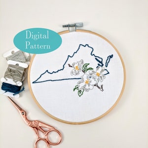 May include: Embroidered outline of the state of Virginia with white flowers and green leaves in a wooden embroidery hoop. The text "Digital Pattern" is in a blue oval above the hoop. There are also embroidery floss and scissors on a white surface.