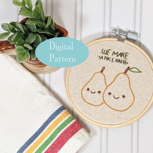 May include: A digital embroidery pattern featuring two pears with smiling faces and the text "We make a nice pair." The pears are embroidered on a beige fabric in a wooden embroidery hoop.