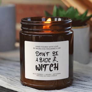 May include: A brown glass candle jar with a white label that reads "HAND POURED WITH LOVE BY MONCIONI FRAGRANCE LAB DON'T BE A BASIC WITCH ECO FRIENDLY | VEGAN | ARTISANAL NATURAL SOY WAX CANDLE".