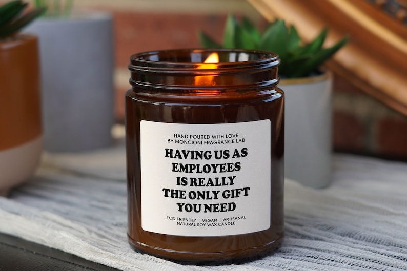 A lit candle in a brown jar with a white label with black text