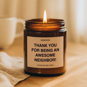 May include: A lit brown glass jar candle with a white label that reads "THANK YOU FOR BEING AN AWESOME NEIGHBOR!". The candle is labeled "MONCIONI" and "Scented Soy Wax Candle". The candle sits on a wooden surface.