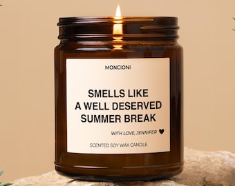 May include: A brown glass candle with a white label that reads "Smells Like A Well Deserved Summer Break" with the text "With Love, Jennifer" and "Scented Soy Wax Candle" below.
