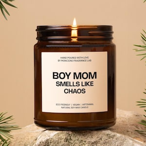 May include: A brown glass candle jar with a white label that reads "BOY MOM SMELLS LIKE CHAOS". The label also says "HAND POURED WITH LOVE BY MONCIONI FRAGRANCE LAB" and "ECO FRIENDLY | VEGAN | ARTISANAL NATURAL SOY WAX CANDLE".