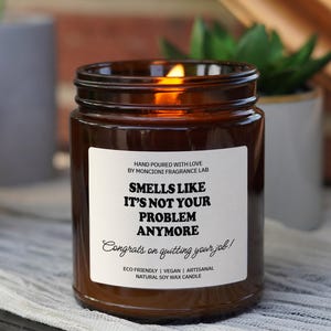 May include: A brown glass candle with a white label that reads "Smells like it's not your problem anymore. Congrats on quitting your job!"  The candle is eco-friendly, vegan, and made with natural soy wax.