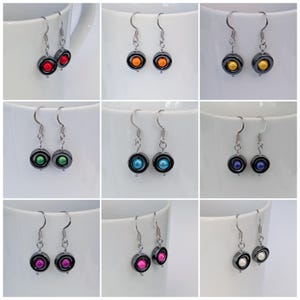 May include: A set of ten pairs of earrings with a black hematite setting and a single coloured bead in the centre. The colours of the beads are red, orange, yellow, green, blue, teal, purple, pink, white, and black.
