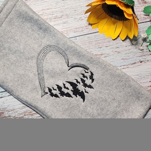 May include: A gray fleece blanket with a black embroidered heart design. The heart is filled with a pattern of bats.