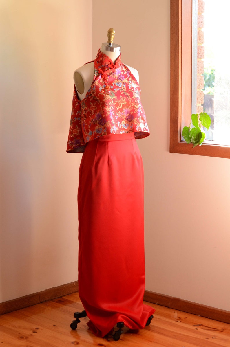 May include: A red halter top with a floral pattern and a matching red skirt. The top has a mandarin collar and a high neckline. The skirt is floor-length and has a fitted silhouette.