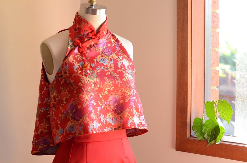 May include: A red halter top with a floral pattern and a mandarin collar. The top is made of a silky fabric and has a cropped length.