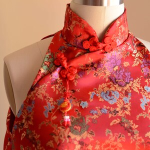 May include: Red halter top with a floral pattern and a mandarin collar. The top has a decorative knot and tassel.