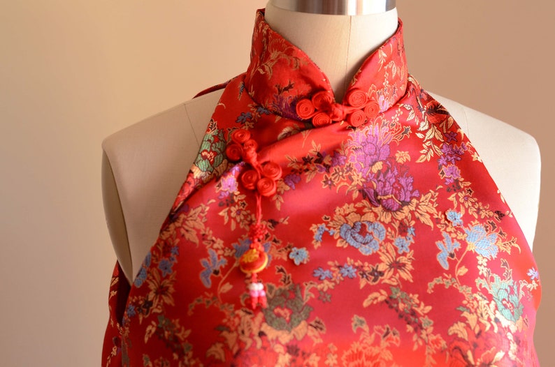 May include: Red halter top with a floral pattern and a mandarin collar. The top has a decorative knot and tassel.