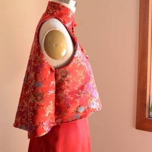 May include: A red sleeveless top with a floral pattern and a mandarin collar. The top is made of a silky fabric and has a cropped length.