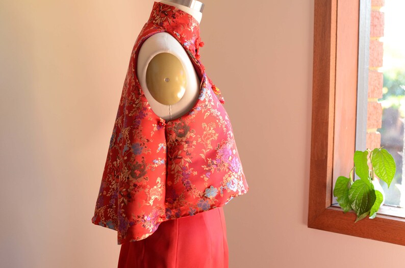 May include: A red sleeveless top with a floral pattern and a mandarin collar. The top is made of a silky fabric and has a cropped length.