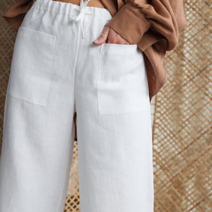 Può includere: Pantaloni bianchi in lino con vita a coulisse e tasche laterali. I pantaloni hanno una gamba larga e una lunghezza a metà polpaccio.