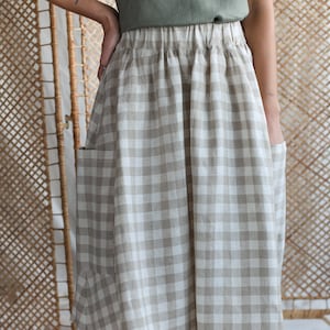 Pode incluir: Saia até ao joelho com padrão xadrez vichy bege e branco. A saia tem cós franzido e dois bolsos grandes. A modelo também usa um top verde. A saia é feita de tecido leve.