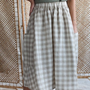 Può includere: Una gonna a quadri vichy beige e bianca con tasche. La gonna ha una vita arricciata e una silhouette fluida.