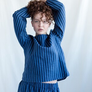 May include: A long-sleeved top and matching bottoms featuring a vertical striped pattern in alternating shades of dark blue and medium blue. The top has a round neckline and loose-fitting sleeves, while the bottoms feature an elasticized waistband.