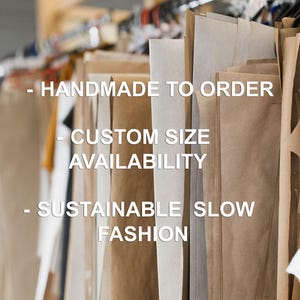 May include: Multiple large sheets of brown and white paper patterns hanging on a clothing rack. The text on the image reads: - HANDMADE TO ORDER - CUSTOM SIZE AVAILABILITY - SUSTAINABLE SLOW FASHION. The patterns are suspended from black hangers.