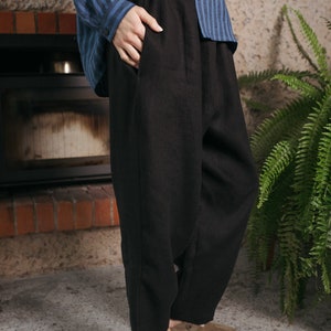 Puede incluir: Pantalón de lino negro de pierna ancha y corte holgado. El pantalón tiene una cintura con cordón y se lleva con zuecos de cuero marrón.