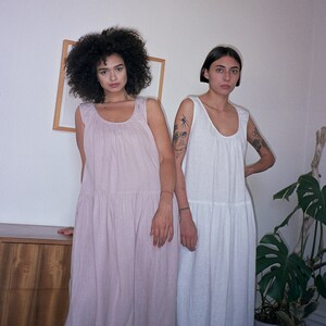 May include: Two people wearing long, flowy dresses. The person on the left is wearing a light pink dress and the person on the right is wearing a white dress.