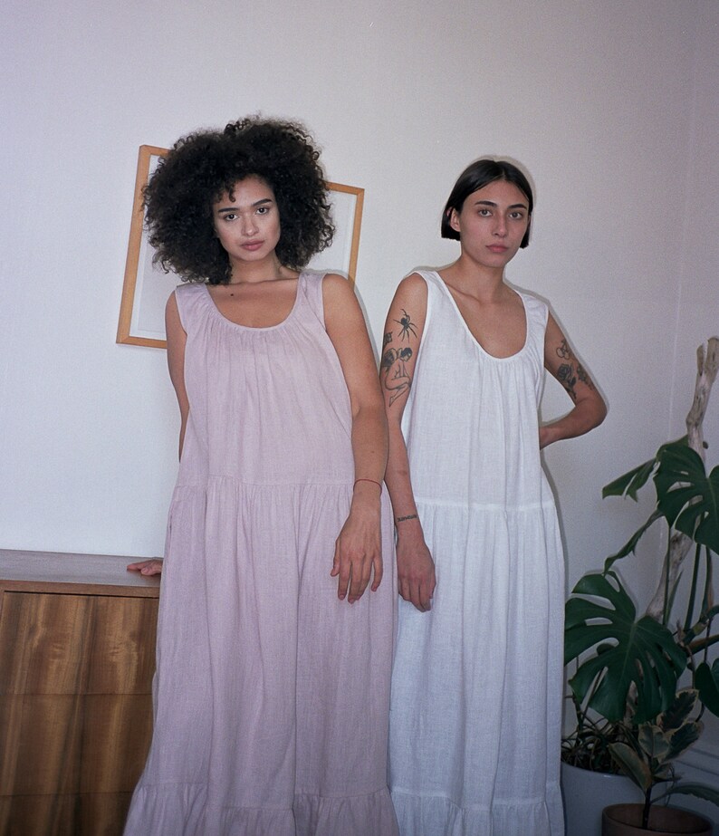 May include: Two people wearing long, flowy dresses. The person on the left is wearing a light pink dress and the person on the right is wearing a white dress.