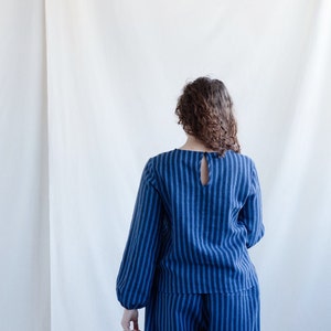 May include: A long-sleeved top and matching pants set featuring a vertical dark blue and light blue striped pattern. The top has a round neckline with a small keyhole opening at the upper back, secured by a single button closure at the nape.