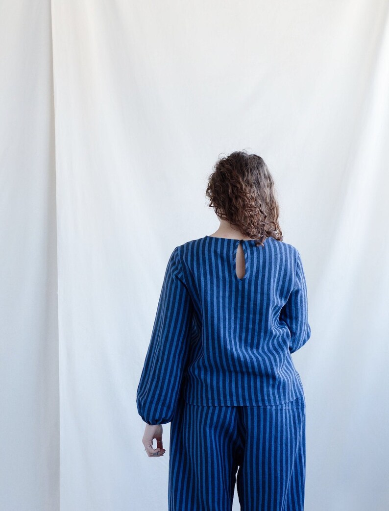 May include: A long-sleeved top and matching pants set featuring a vertical dark blue and light blue striped pattern. The top has a round neckline with a small keyhole opening at the upper back, secured by a single button closure at the nape.