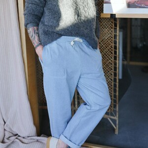 May include: A person wearing a gray fuzzy sweater and light blue pants with a drawstring waist. The person is also wearing white sneakers with brown soles. The pants are cuffed at the ankles.