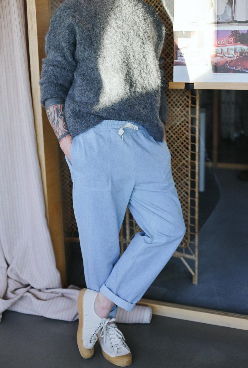 May include: A person wearing a gray fuzzy sweater and light blue pants with a drawstring waist. The person is also wearing white sneakers with brown soles. The pants are cuffed at the ankles.